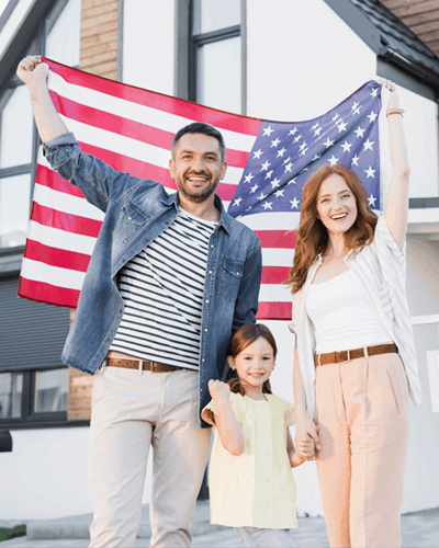 family and daughter holding an American flag standing beside the new home that they purchased